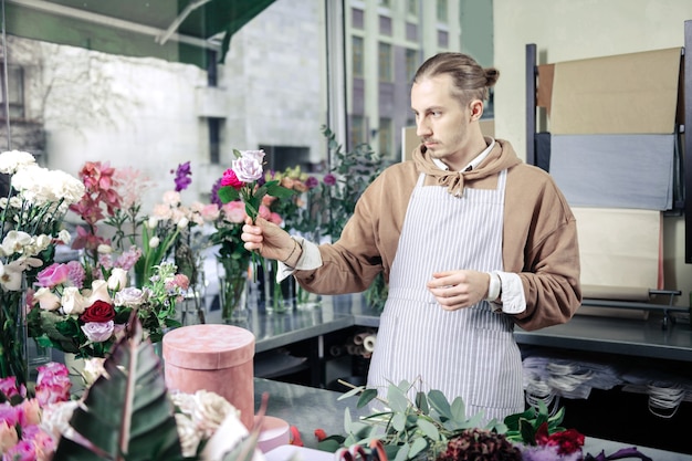 Dar uma olhada. Florista elegante e bonita usando avental enquanto trabalha em uma floricultura