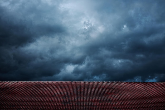 Dark Dramatic Sky before Rain and Storm Cyclone kommt mit Black Windy Cloud House Cover by Red Tiles Roof als Wetter- und Jahreszeitenwechsel im Vordergrund