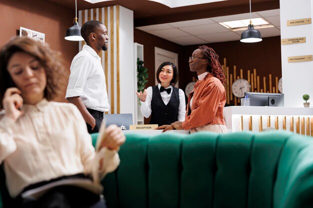 Das asiatische Hotelpersonal begrüßt die Gäste in der Lobby und bietet exzellenten Service und Unterstützung an der Rezeption. Eine Angestellte spricht mit einem Paar, das im Hotel ankommt, beim Einchecken an der Rezeption.