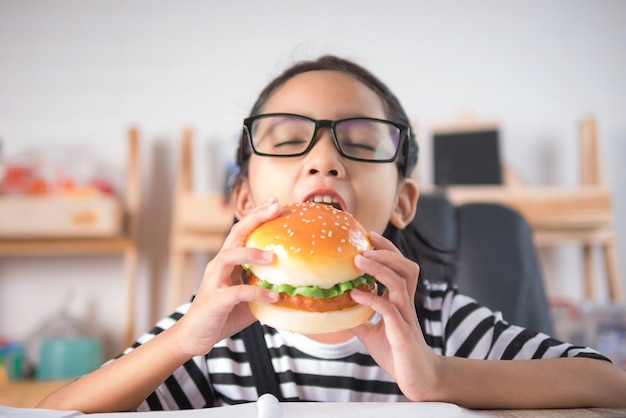 Das asiatische kleine Mädchen, das Hamburger auf Holztisch isst, wählen flache Schärfentiefe des Fokus aus