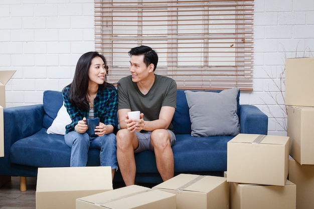 Das asiatische Paar sitzt auf einem Sofa und ist gerade in ein neues Zuhause gezogen, um eine herzliche Familie zu gründen.