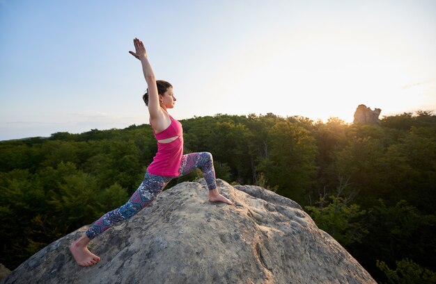 Das attraktive dünne Mädchen, das das Ausdehnen von Yoga tut, trainiert oben auf enormen Felsen