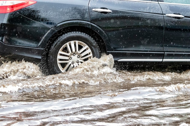 Das Auto fährt bei starkem Regen durch eine Pfütze Wasserspritzer unter den Rädern eines Autos Überschwemmungen und Hochwasser in der Stadt