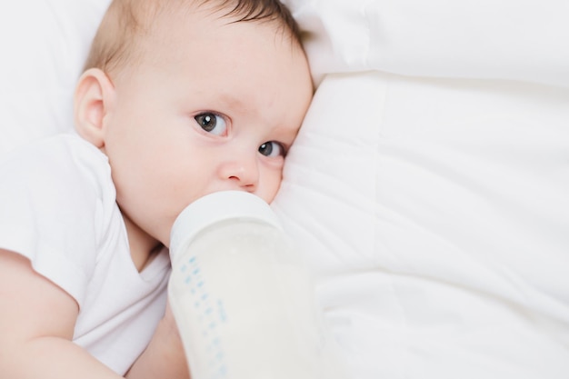 Das Baby in seiner Krippe isst aus einer Flasche Babynahrung copyspace Künstliche Fütterung