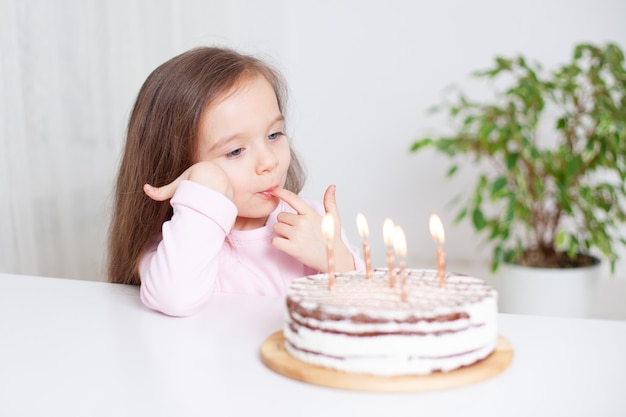 Das Baby isst Kuchen an seinem Geburtstag Kerzen auf dem Kuchen brennen Ein süßes europäisches Mädchen