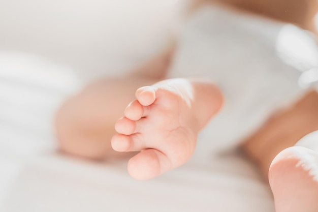 Das Baby kriecht auf einem weißen Bett Beine eines Neugeborenen sehen gerade aus Babypflege