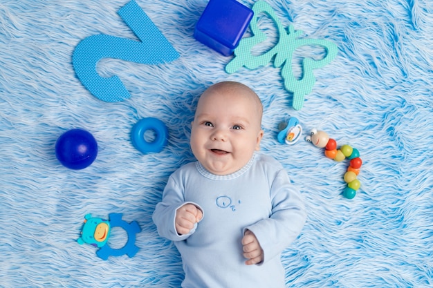 Das Baby liegt zu Hause auf einer blauen Matte zwischen Spielzeug, dem Konzept der Entwicklung und Spielen and
