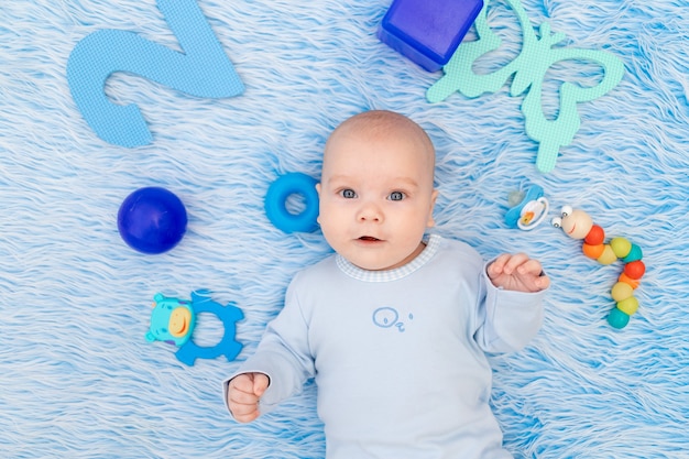 Das Baby liegt zu Hause auf einer blauen Matte zwischen Spielzeug, dem Konzept der Entwicklung und Spielen