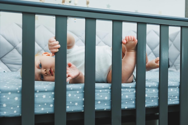 Das Baby schaut durch die Seiten der Wiege in das Zimmer ein kleiner neugeborener Junge liegt in einer Wiege für Kinder ein Platz für Kinder zu schlafen