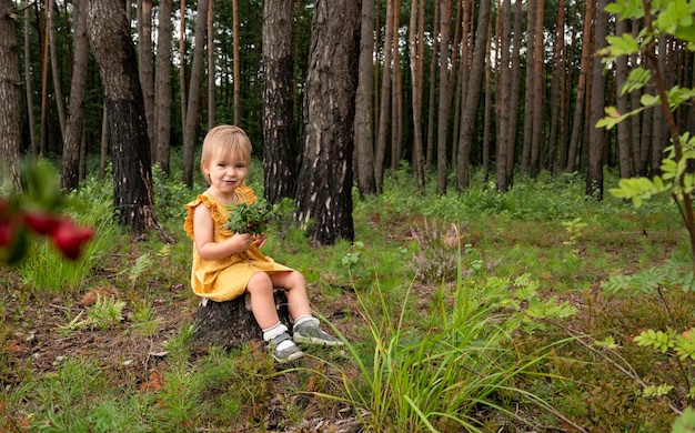 Das Baby sitzt im Wald auf einem Baumstumpf und isst Preiselbeeren