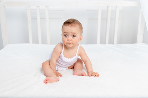 Das Baby sitzt in einem Kinderbett in einem hellen Raum