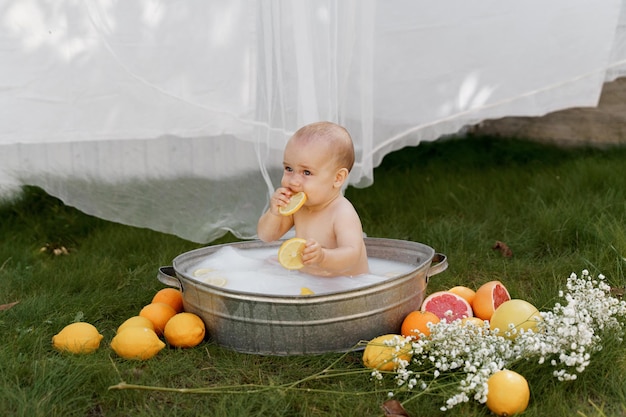 das baby sitzt in einer wanne auf dem gras im hof