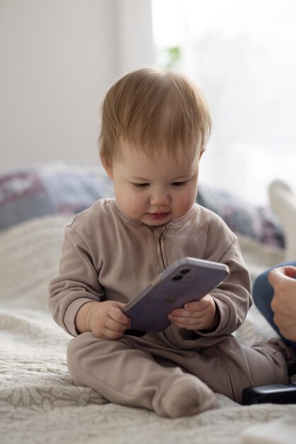 Das Baby sitzt mit seiner Mutter auf dem Bett und schaut interessiert auf ihr Smartphone