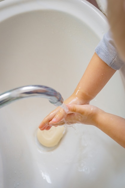 Das Baby spült sich den Schaum von den Händen, die Seife liegt im Waschbecken.