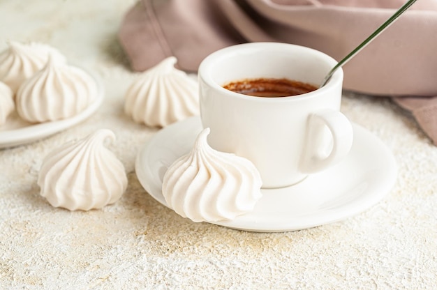 Das baiser liegt auf einem teller neben einer tasse kaffee. im hintergrund ein teller mit baiser und einer serviette. heller hintergrund.