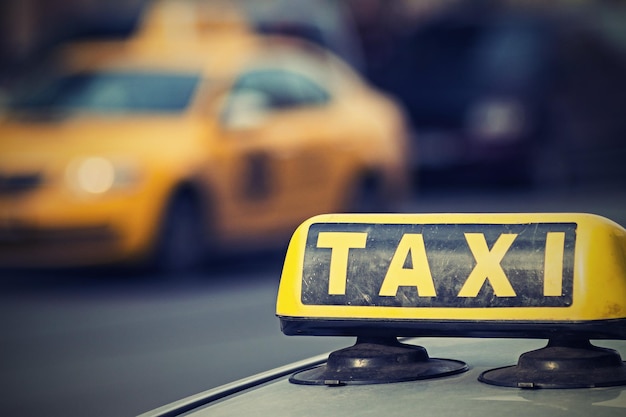Das Bild eines Zeichens einer Taxinahaufnahme auf einem undeutlichen Hintergrund des Autos eines Taxis gelb
