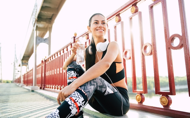 Das bisschen Wasser bei Sportübungen. Frau trinkt Wasser, während sie sich nach dem Morgenlauf ausruht