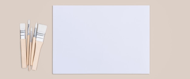 Das Blatt ist reinweiß und die Pinsel befinden sich auf einem beigen Hintergrund mit einem Platz zum Kopieren.