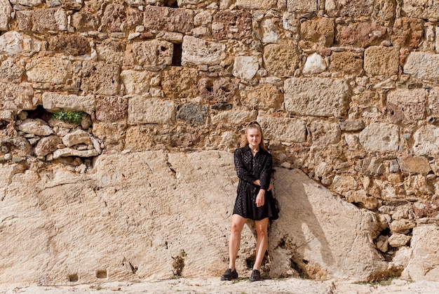 Das blonde Mädchen schaut links im schwarzen Kleid auf Steinhintergrund