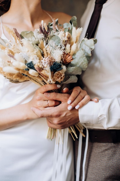 Foto das brautpaar hält einen wunderschönen strauß getrockneter blumen im boho-stil in den händen