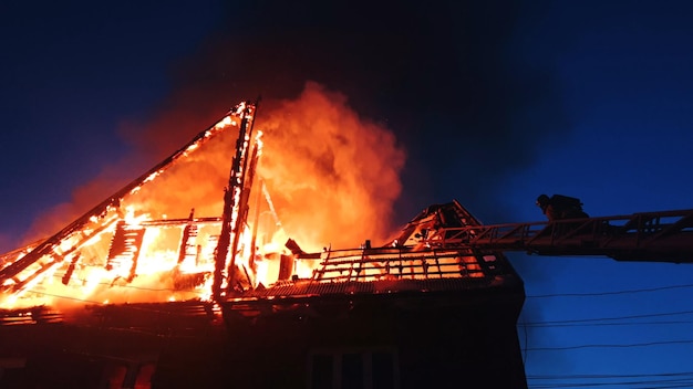 Das Dach des Hauses brennt Das Wohnhaus brennt Dorf Feuerwehrleute löschen ein Feuer vom Kran von oben Rauch und Funken