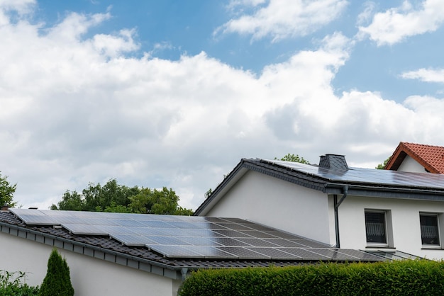 Das Dach eines Wohngebäudes ist mit Sonnenkollektoren bedeckt und lässt weiße Wolken am Himmel aufleuchten