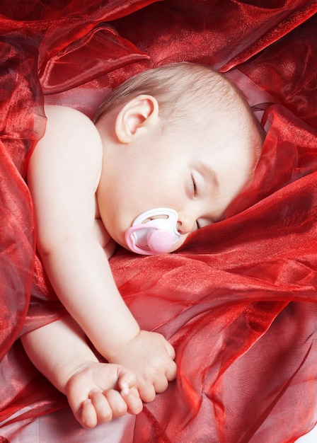 Das einjährige Baby schläft und ist in rotes Kalikomaterial eingewickelt. Nahansicht.