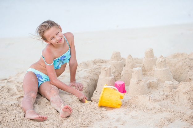 Das entzückende kleine Mädchen, das mit Strand spielt, spielt auf weißem tropial Strand