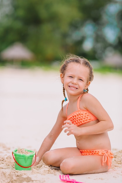 Das entzückende kleine Mädchen, das mit Strand spielt, spielt während der tropischen Ferien