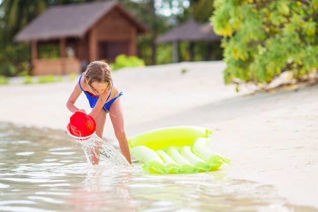 Das entzückende kleine Mädchen, das mit Strand spielt, spielt während der tropischen Ferien