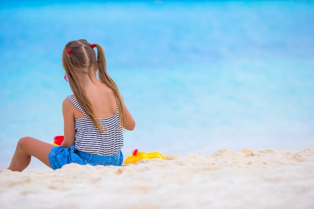 Das entzückende kleine Mädchen, das mit Strand spielt, spielt während der tropischen Ferien