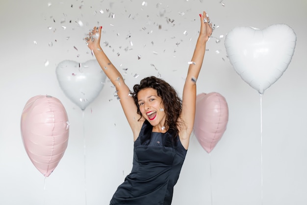 Das Erfolgsgefühl. Glückliches sexy Brunettemädchen, das das Feiern mit Konfetti und Herzballons auf einem weißen Hintergrund genießt.