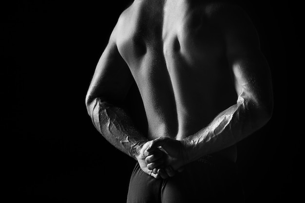 Das farblose Bild der Rückseite des Torsos des attraktiven männlichen Bodybuilders auf schwarzem Studiohintergrund.
