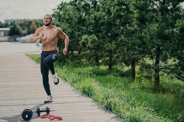 Das Foto eines gesunden, motivierten Mannes mit dicken Borstenübungen im Freien springt und führt zu einem gesunden Lebensstil, der in der Nähe von Sportgeräten posiert, hat einen starken muskulösen Körper Fitness-Sport- und Trainingskonzept