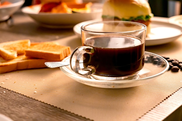 Das Frühstück und heißer schwarzer Kaffee auf dem Holztisch mit einem Sonnenstrahl am Morgen.