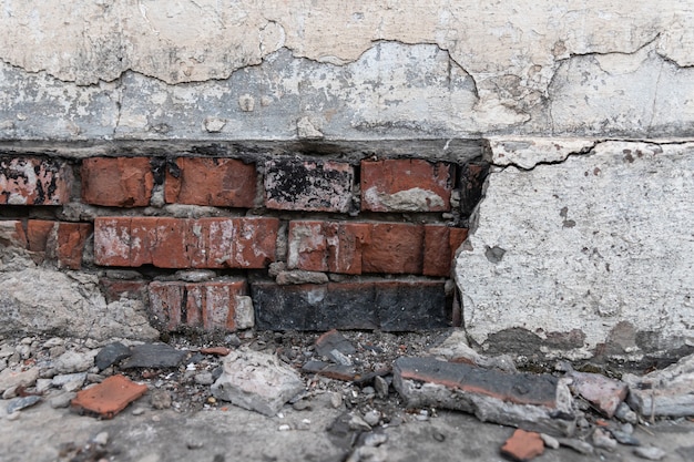 Das Fundament eines Wohngebäudes bricht allmählich zusammen. Risse im Fundament. Verputz, der durch Witterungseinflüsse von einer Mauer fällt.