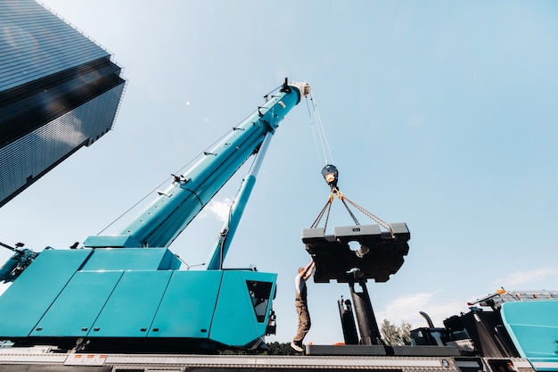 Das Gegengewicht wird von einem nicht erkennbaren Arbeiter an einem großen blauen Autokran installiert und ist bereit, auf einer Baustelle zu arbeiten