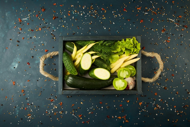 DAS GEMÜSE IM KASTEN AUF DEM STEIN EIN DUNKEL. JUNGE KRÄUTER ZWIEBEL KNOBLAUCH GRÜNE BOHNEN GELBE MAIS ZUCCHINI HELL GEWÜRZE SIND IN EINER HOLZKISTE MIT SEILGRIFFEN AUF EINER DUNKELEN STRUKTURIERTEN.