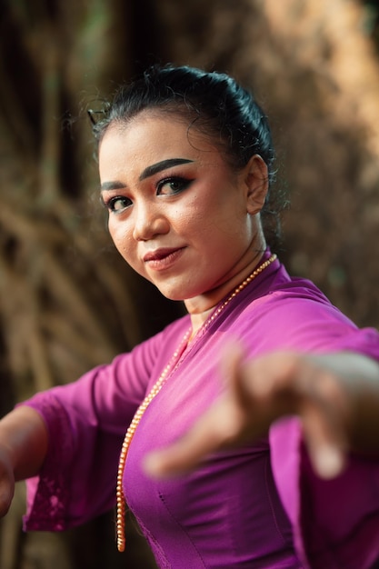 Das Gesicht einer javanischen Frau mit Make-up und einem traditionellen lila Kleid namens Kebaya, während sie mit Schmuck am Hals tanzt und posiert