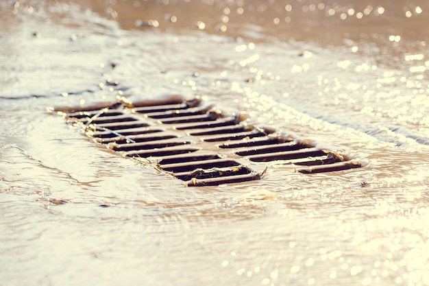 Foto das gitter des regenwasserkanals nach dem regen das wasser fließt in den regenwasserabfluss selektiver fokus defokussierter hintergrund