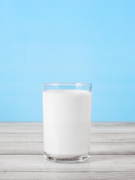 Das Glas voll Milch auf Holztisch Glas frische weiße Milch auf blauem Hintergrund in der Küche