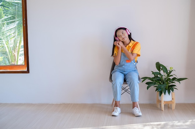 Das glückliche Mädchen, das auf einem Stuhl sitzt und Musik in einem minimalen Raum zu Hause hört