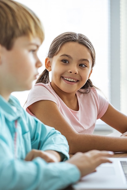 Das glückliche Mädchen und ein Junge mit einem Laptop am Tisch sitzen