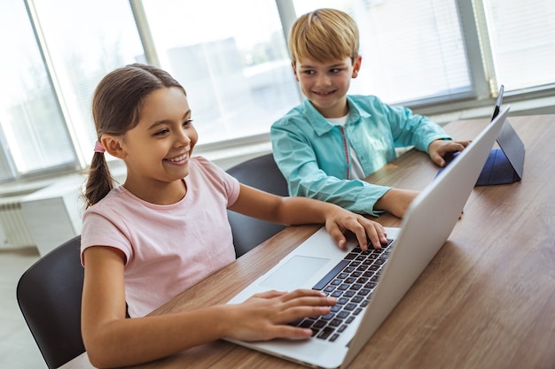Das glückliche Mädchen und ein Junge mit Gadgets sitzen am Schreibtisch