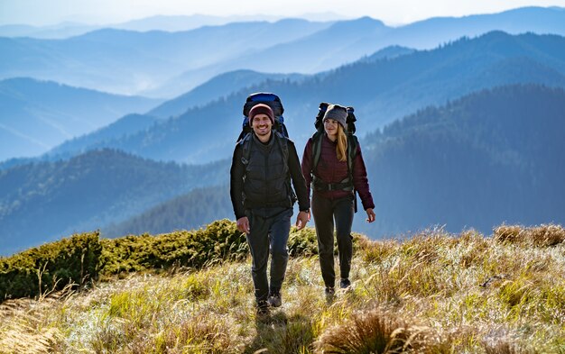 Das glückliche Paar mit Rucksäcken zu Fuß zum Berg