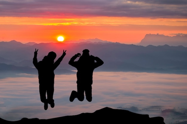 Das glückliche Paar springend auf den Berg auf der Sonnenaufgangzeit. Leute, die Spaß draußen haben. Konzept der freundlichen Familie.