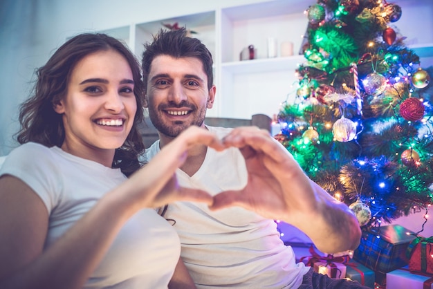 Das glückliche Paar zeigt das Herzsymbol neben dem Weihnachtsbaum