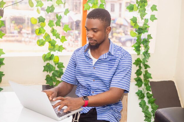 Das glückliche und lächelnde Gesicht des afrikanischen Mannes arbeitet am Laptop im Café