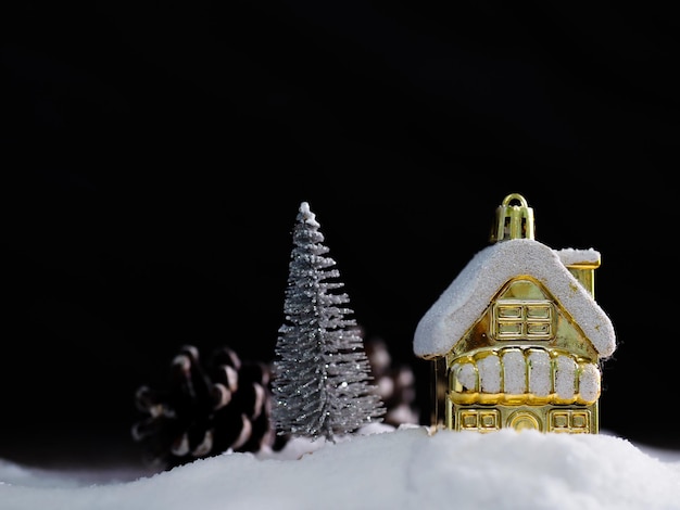 Das goldene Haus war mit weißem Schnee und einem silbernen Weihnachtsbaum an der Seite mit verschwommenen Tannenzapfen auf schwarzem Hintergrund bedeckt. Happiness of Christms and New Year Concept