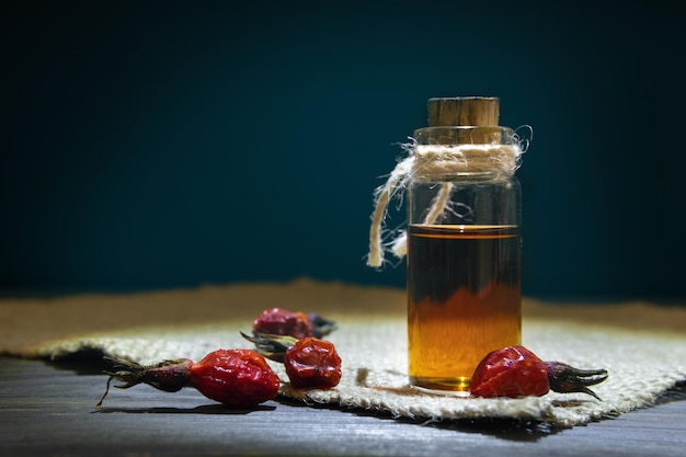 Das Hagebuttenöl auf Holzbrettern vor dunklem Hintergrund Flasche mit einer Schnur mit ätherischem Heckenrosenöl